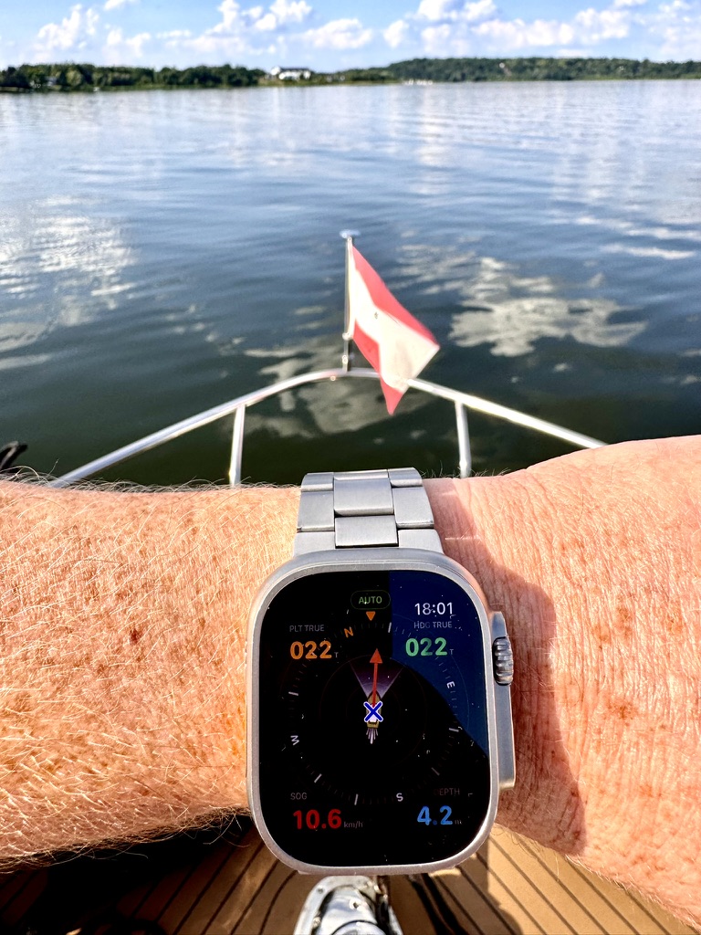 Apple Watch mit Rivers & Seas und aktivem Autopiloten am Steuerstand eines Motorboots.